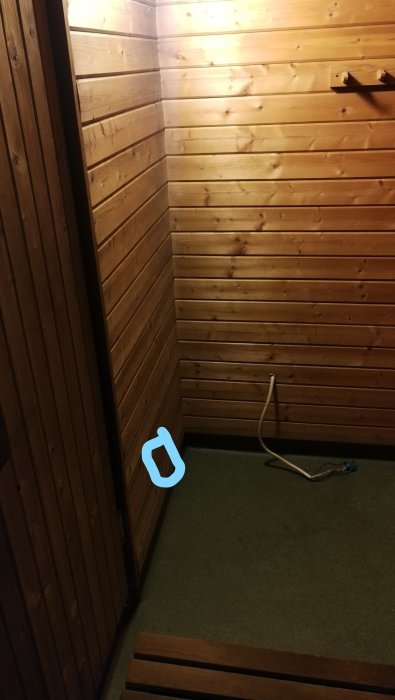 Träpanelklädd bastu med tom hörna där vedkamin varit, ställning för bastuaggregat, kabel på golvet.