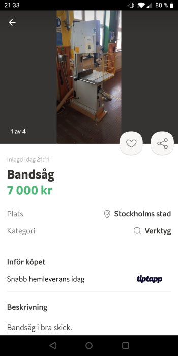 Stående bandsåg i arbetslokal, grå och vit med säkerhetsskärm, märkt 7 000 kr i bra skick.