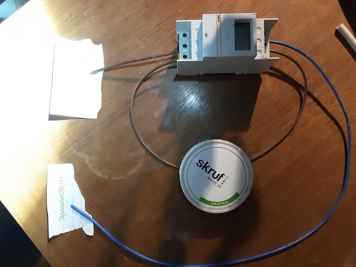 Elektrisk installationsutrustning bredvid en snusdosa med kabel kopplad, på ett bord.
