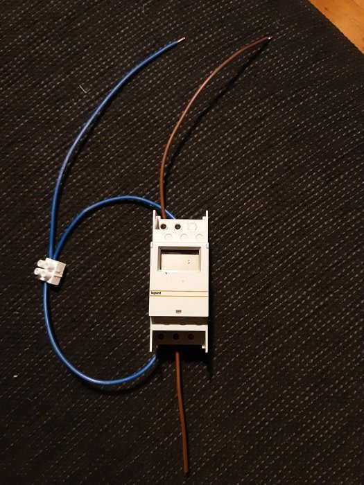 Automatsäkring med blå och brun ledning på mörk textilbakgrund.