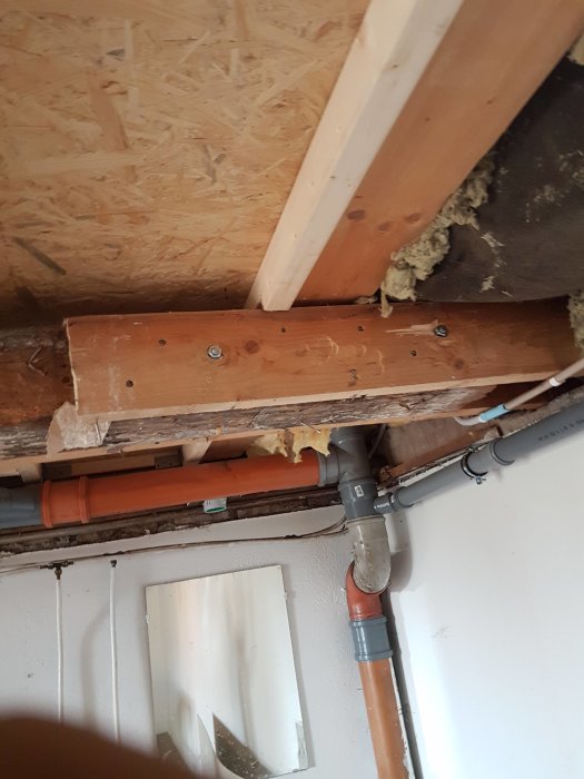 Överblick av ett garage med synliga träbalkar och rörsystem, visar en träbalk förstärkt med en limträbalk och isolering som hänger löst.