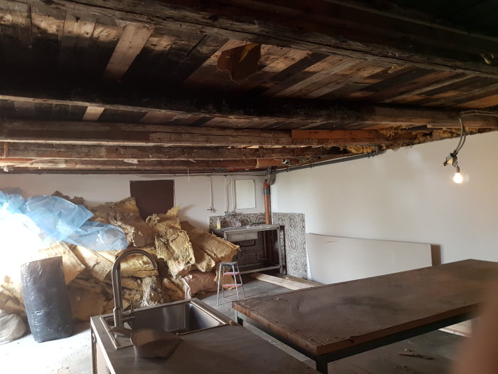 Gamla exponerade takbjälkar i garage med borttagna gips och isolering, renoveringsavfall synligt.