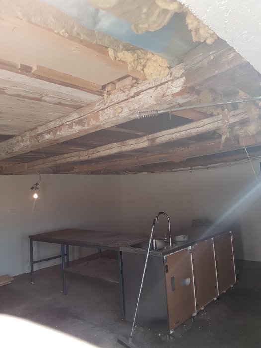 Gammalt träbjälklag i garage som behöver förstärkas, synlig isolering och temporär stödåtgärd.