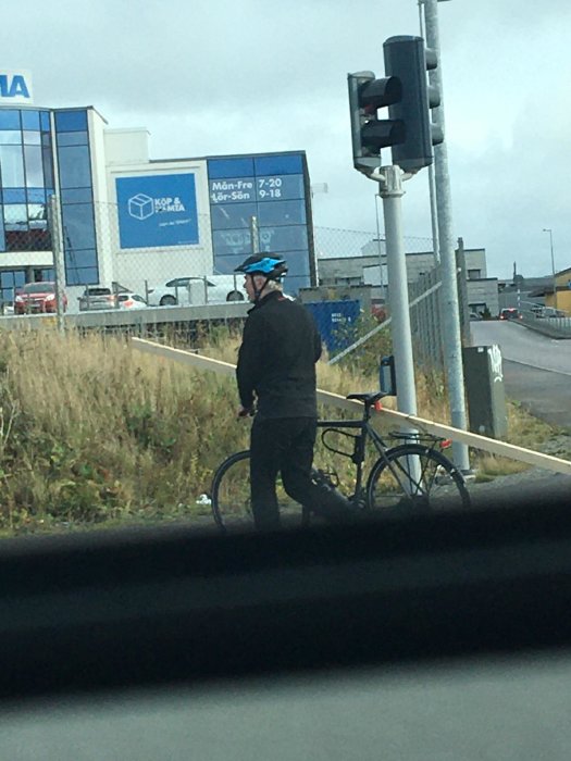 Person med hjälm står bredvid cykel vid övergångsställe, IKEA-varuhus i bakgrunden.