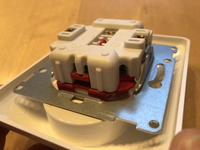 Närbild av en öppen elektrisk kopplingsplint i ett vägguttag där någon håller i höljet.