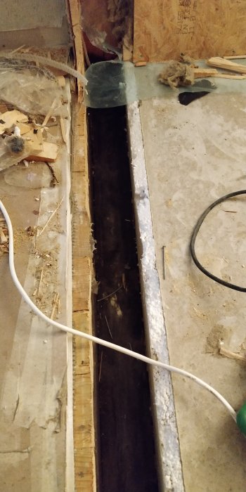 Upprivet golv visar ett 22cm djupt och 11cm brett utrymme mellan gammal och ny byggnad, kantad av timmer och betong.