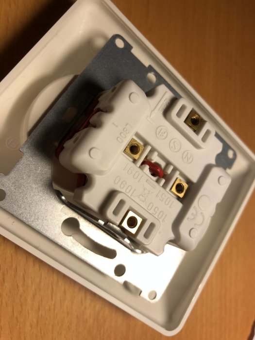 Öppen elektrisk vägguttag med trådar som är fastklämda och inte kan dras ut.