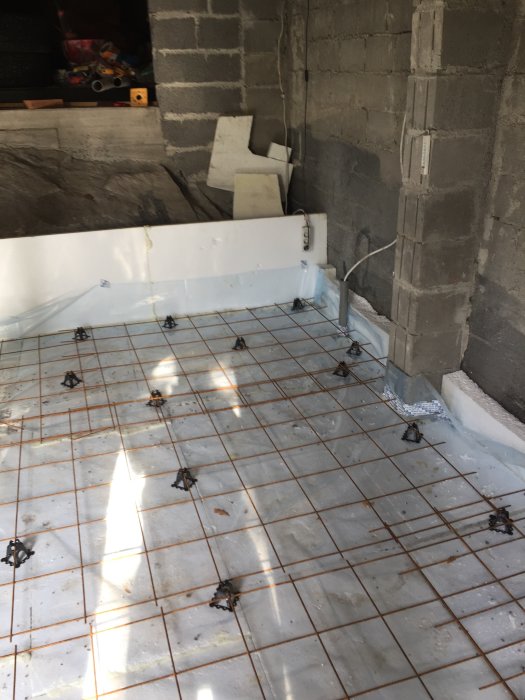 Utomhusverkstad under konstruktion med nylagd fuktspärr och armeringsnät på betonggolv.