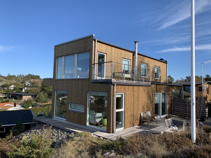Moderna hus med Kebony-paneler och stora fönster mot klarblå himmel.