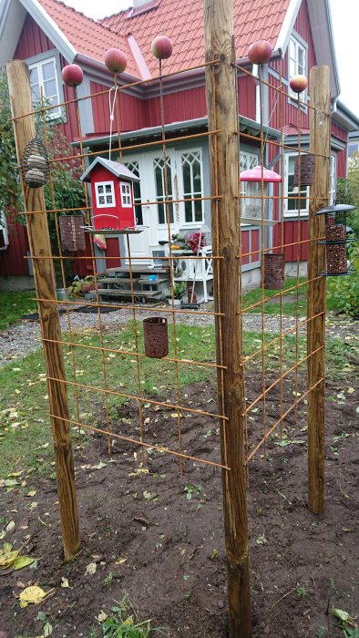 Tillfällig fågelmatningsstation med stolpar och armeringsnät i en trädgård, röda hus i bakgrunden.