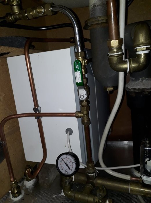 Värmepanna under diskbänk omgiven av rördragningar och manometer.