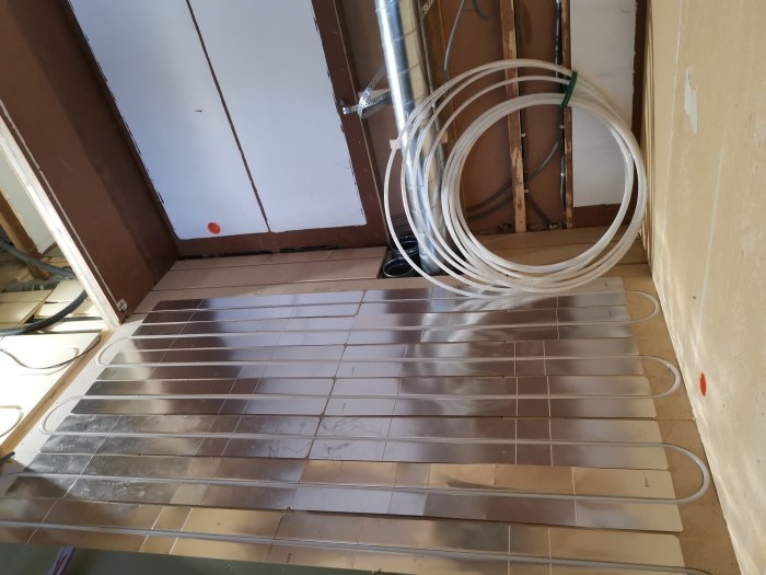 Installation av golvvärme med synliga värmeslingor utlagda på ett golv under renovering.