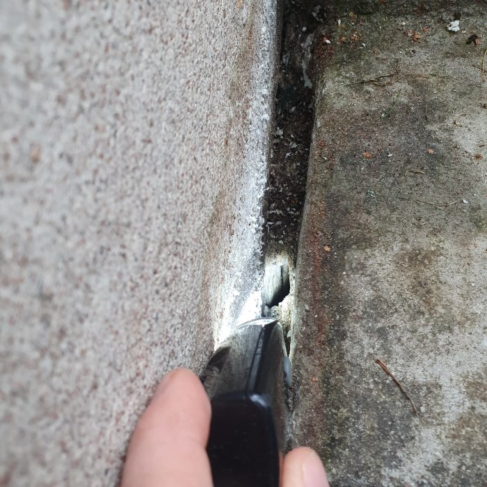 Närbild av en hand som håller en ficklampa och belyser springan mellan en betongvägg och en källartrappa.