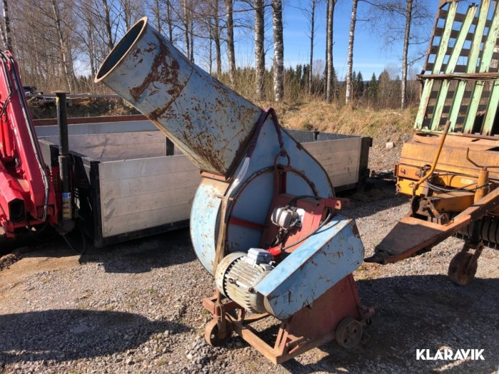 En gammal, rostig hökanon utomhus med en uppfälld utkastarrör, framför andra lantbruksmaskiner.