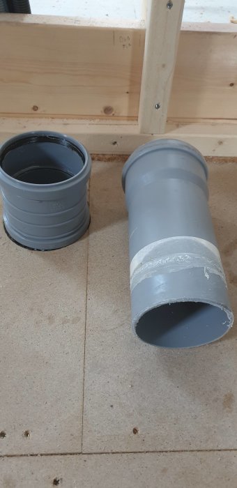 Ett 110 mm PVC-rör med muff och en separat dubbelmuff på ett bygggolv.