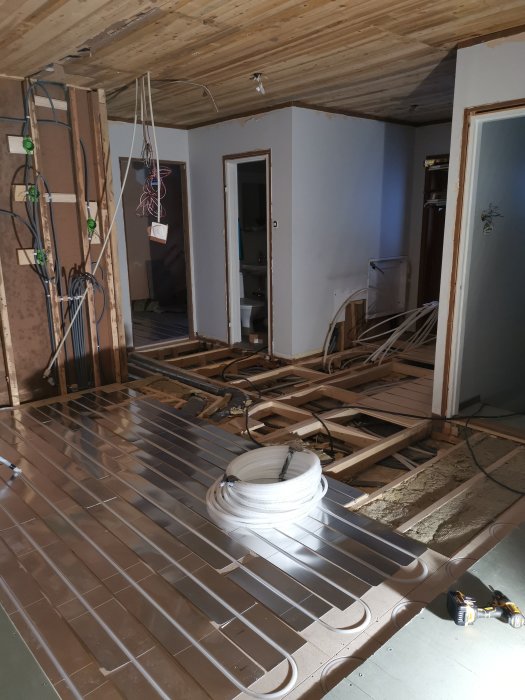 Renoveringsarbete av en hall med ofärdiga golv och väggar, synliga rör och elledningar.