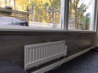 Nyinstallerade lister och en fönsterbräda ovanför en radiator, med laminatvägg och ett fönster med utsikt mot träd.