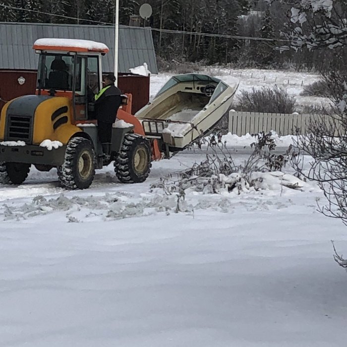 Traktor med frontlastare som transporterar en båt i vinterlandskap.