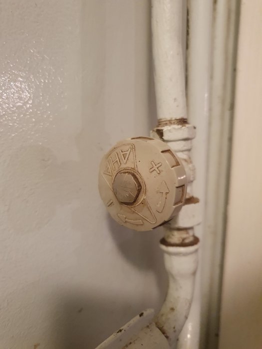 Gammalt radiatorvred märkt "AHA" monterat på en vit element med tecken av slitage och färgskikt.