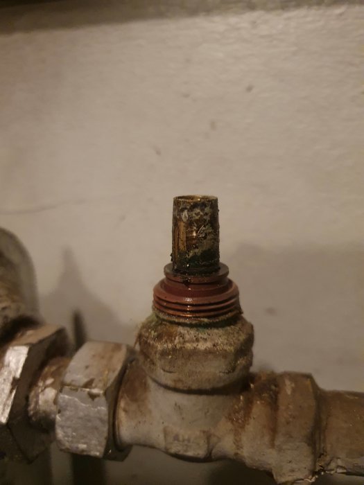 En uppåtböjd ventilaxel på en rördel, omgiven av skruv och mutter, med synlig korrosion.