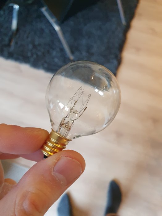 Hand håller en 7W glödlampa mot golv med matta i bakgrunden.