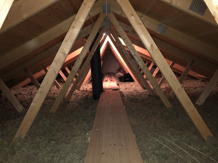 Lågt tak i en kallvind med synliga takstolar, isolering mellan sparrarna och en smal gångplanka längs mitten.