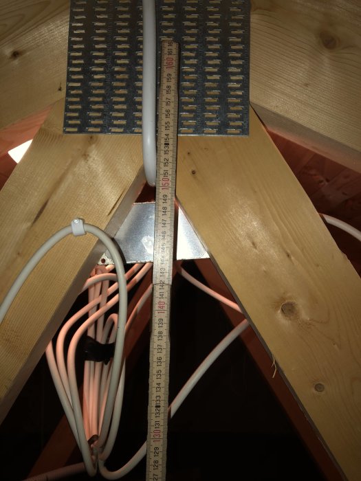 Måttband visar takhöjd på vinden mellan träbjälkar och elektriska kablar, potentiellt för ombyggnad till lekrum.