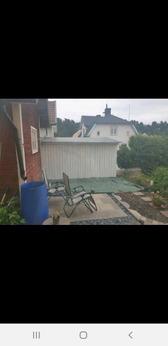 Nymålat plank och anlagd uteplats med stenplattor samt trädgårdsmöbler vid trähus.