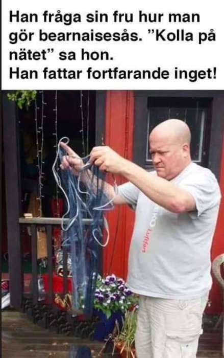 Man förvirrat håller i en röra av nät mot en bakgrund av ett trähus och blomkrukor.