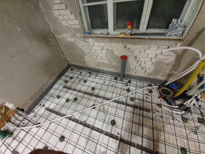 Armeringsnät på badrumsgolv med rörinstallationer, varm- och kallvattenledningar samt tomrör längs väggen.