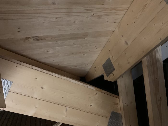 Träkonstruktion av takstolar med synligt råspont och metallbeslag i en takkupa under byggnad.