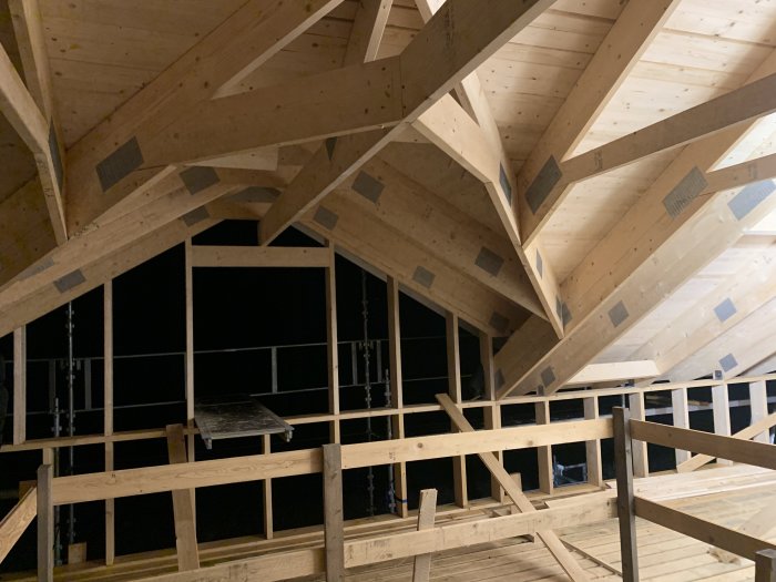 Byggnadsstomme med uppsatta takstolar, råspont och svart byggfolie i ett hus under konstruktion.