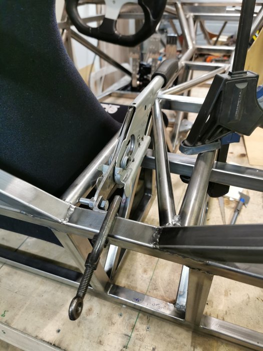 Bild på installationen av en handbromsspak och dess fästen i ett fordonsskelett, närbild med detaljer.