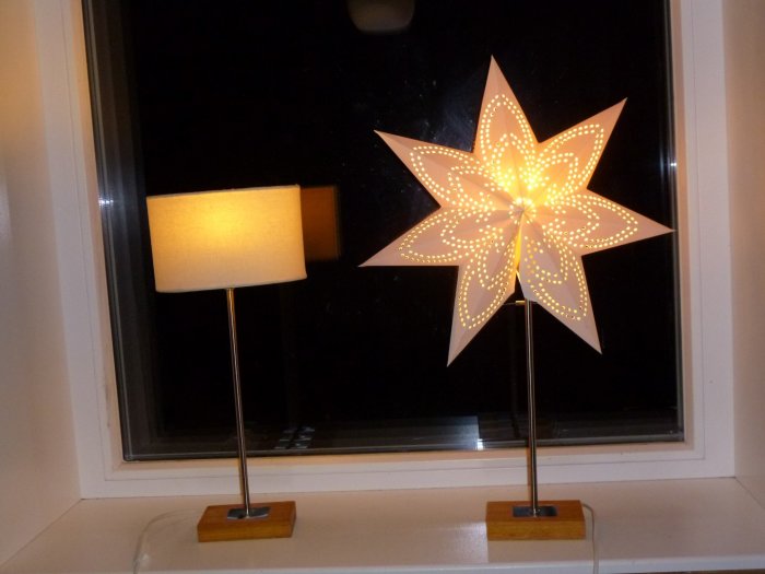 Bordslampor med en traditionell skärm och 7-uddig upplyst adventsstjärna i ett fönster.