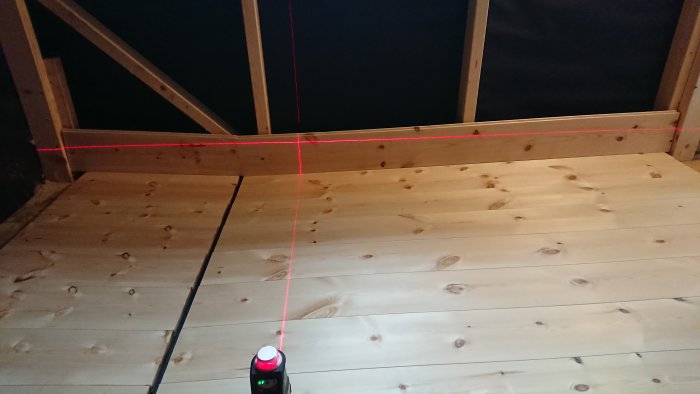 Nyinstallerade furugolvbrädor i bastu med laserlinje för att säkra rätt vinkel.