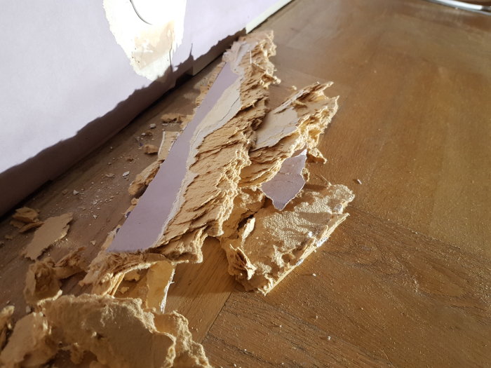 Borttaget material från en vägg som visar lager av kartongliknande material och spontat trä under renovering.