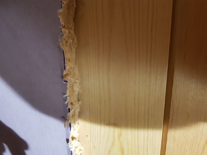 Närbild på ett dörrhål med kartongliknande material framför spontat trä.