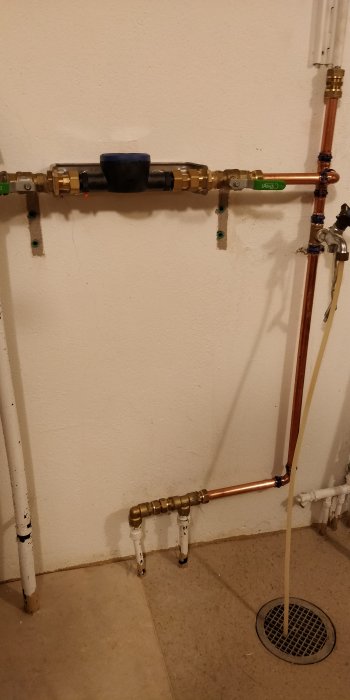 Installation av nya ventiler och kopparrör mot en vit vägg med golvrännan synlig.