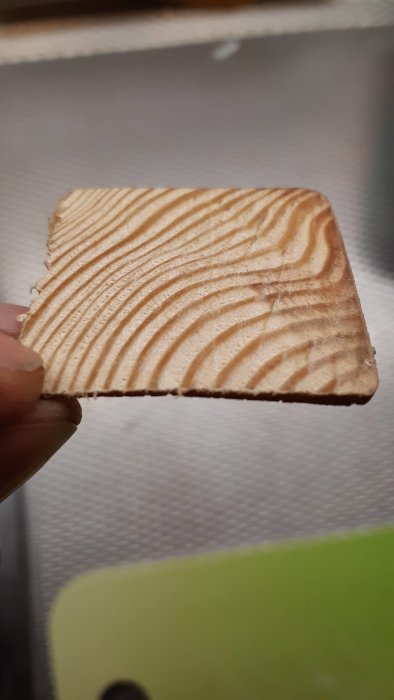 Hand håller en nysågad tunn ekkloss med tydligt ådringsmönster, behandlad med paraffinolja, framför en suddig bakgrund.