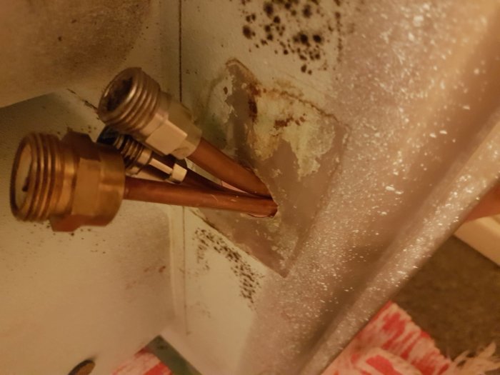 Kopparrör med muttrar under en diskbänk, trånga att passera genom hålet i diskbänksplåten.