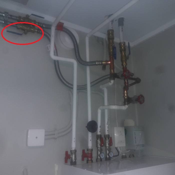 VVS-installation i skåp med rör, kulventil markerad med röd cirkel och olika ventiler.
