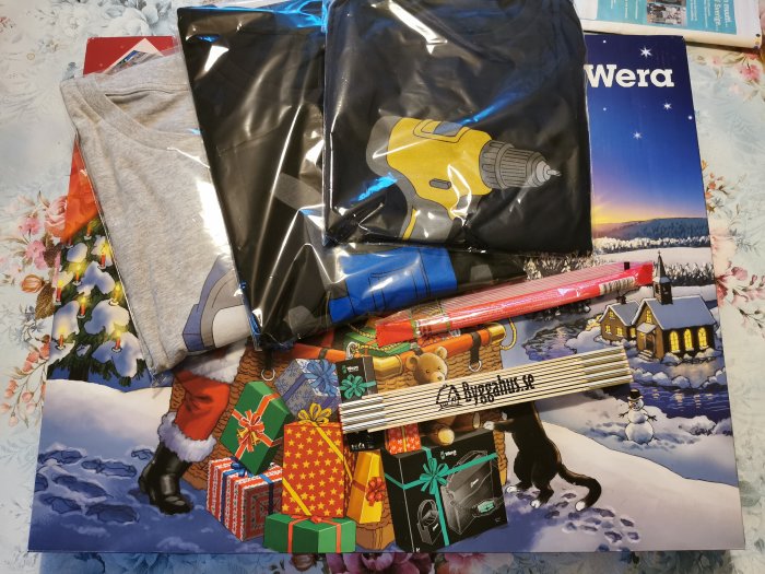 Weras adventskalender och tre olika t-shirts bredvid en tumstock på ett blommigt bord.