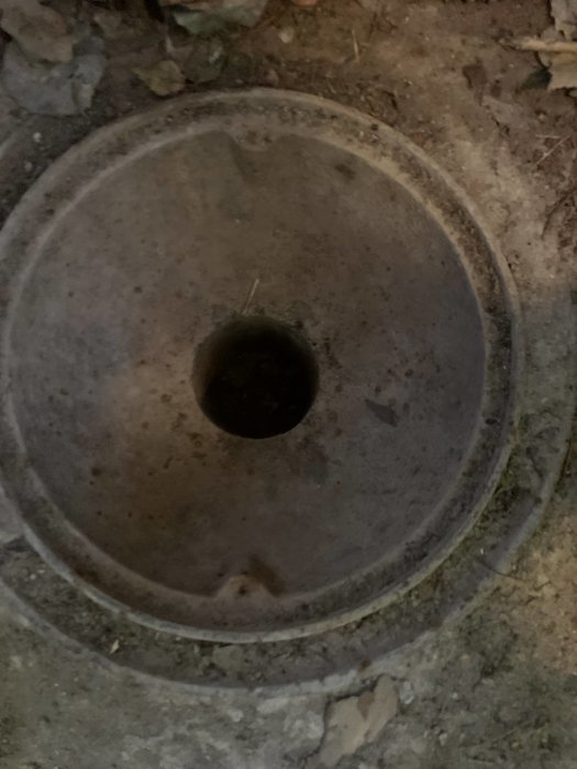 Översikt av en gammal dagvattenbrunn med ett hål i mitten och ett gallerlock runtom.