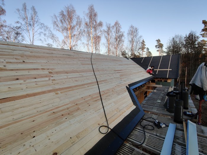 Person som installerar takfotsplåtar och vindskivor på nytt trähus under en klar dag.