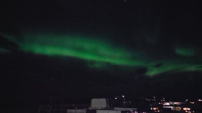 Norrsken i mörk himmel över silhuetten av en byggarbetsplats med byggmaterial och hus i förgrunden.