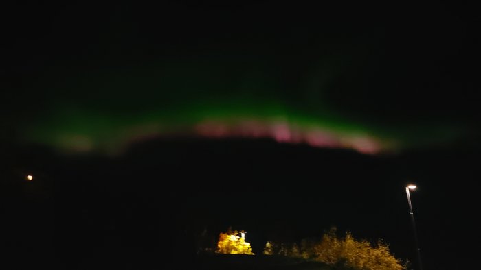 Norrsken i nattsvart himmel över en upplyst byggarbetsplats.