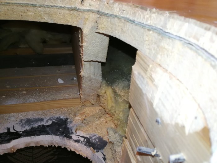 Kapad mellanbjälke i tak med synligt sågspån och isolering för installation av kaminrör.