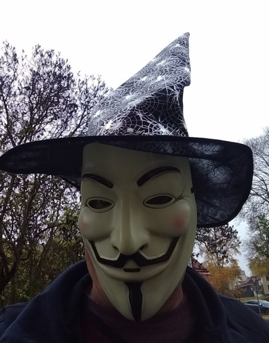 Person bär Guy Fawkes-mask och häxhatt som ansiktsmask utomhus.
