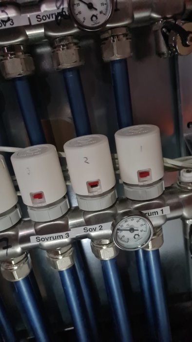 Ventiler med numrerade ställdon och rörledningar, märkta för olika sovrum, bredvid manometer.