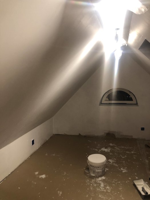 Omålad gipsvägg med synliga pappremsor och bubblor efter spackling, täckt golv och spotlights.